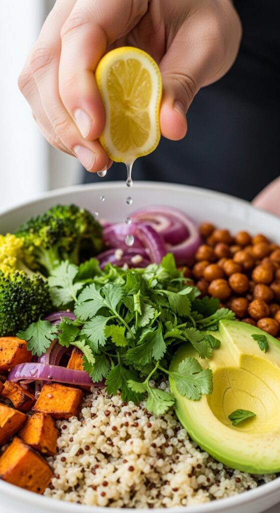 Hands squeezing a lemon wedge over a vibrant grain bowl with roasted veggies, chickpeas, avocado, and fresh herbs in natural daylight